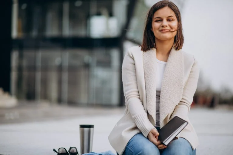 Young girl sitting reading book and drinking coffee outside the street