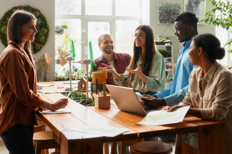 time de 5 pessoas em volta de uma mesa de madeira trabalhando em conjunto